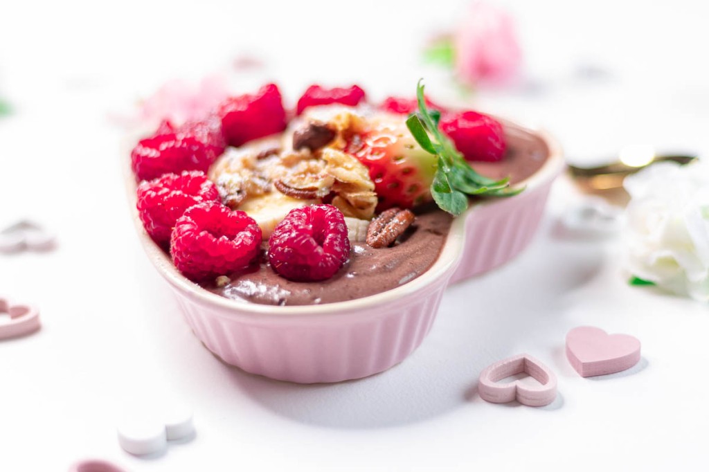 vegan chocolate pudding with cashew yoghurt and raw cacao powder topped with raspberries, strawberries, banana, and nuts